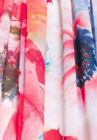 Plis de tissu avec des motifs floraux vibrants en rouge, rose, bleu et blanc, mettant en valeur de grands pétales de fleurs et des centres détaillés.