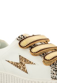 Baskets blanches avec un design en éclair doré pailleté, des brides métalliques dorées et marron, et un accent en imprimé animal texturé.
