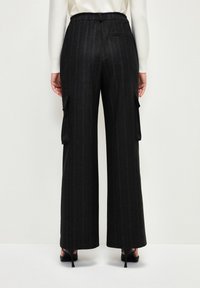 Weite Cargo-Hosen in Dunkelgrau mit weißen Streifen. Mit Seitentaschen und einem elastischen Bund. Kombiniert mit schwarzen High Heels.