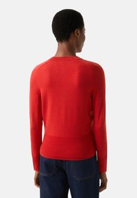 Roter Strickpullover mit langen Ärmeln, rundem Hals und geripptem Saum, mit figurbetonter Silhouette und glatter Textur.