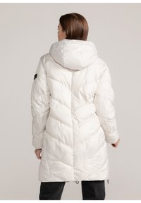 Witte, lange pufferjas met een capuchon, voorzien van een chevron-quiltpatroon en elastische manchetten. Zwarte accenten op de mouwen. Gladde, glanzende textuur.