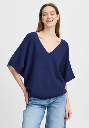Navyblaues, lockeres Stricktop mit tiefem V-Ausschnitt und weiten Ärmeln. Kombiniert mit hellblauen Jeans, die die lässige Kleidung ergänzen.