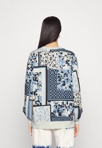 Felpa blu a motif con design floreali, a scacchi e a patchwork. Vestibilità ampia con polsini e orlo a coste, realizzata in tessuto morbido.