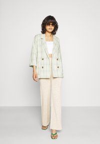 Blazer de xadrez de dois botões em verde menta e bege, combinado com calças largas creme. Modelo usando óculos de sol marrons em formato quadrado e sandálias verdes.