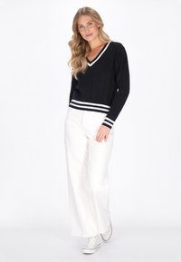 Marineblauwe gebreide trui met een V-hals en een witte gestreepte zoom, gecombineerd met witte wijde broek en witte sneakers.