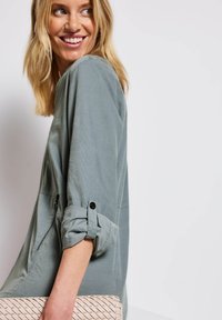 Grå, lätt topp med rullade ärmar och knapppdetaljer, tillsammans med en texturerad, vävd beige clutch. Enkelt, modernt design.