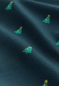 Námornícky textil s textúrovaným povrchom, na ktorom sú malé vyšívané vianočné stromčeky v zelenej farbe s žltými hviezdami a farebnými ozdobami.