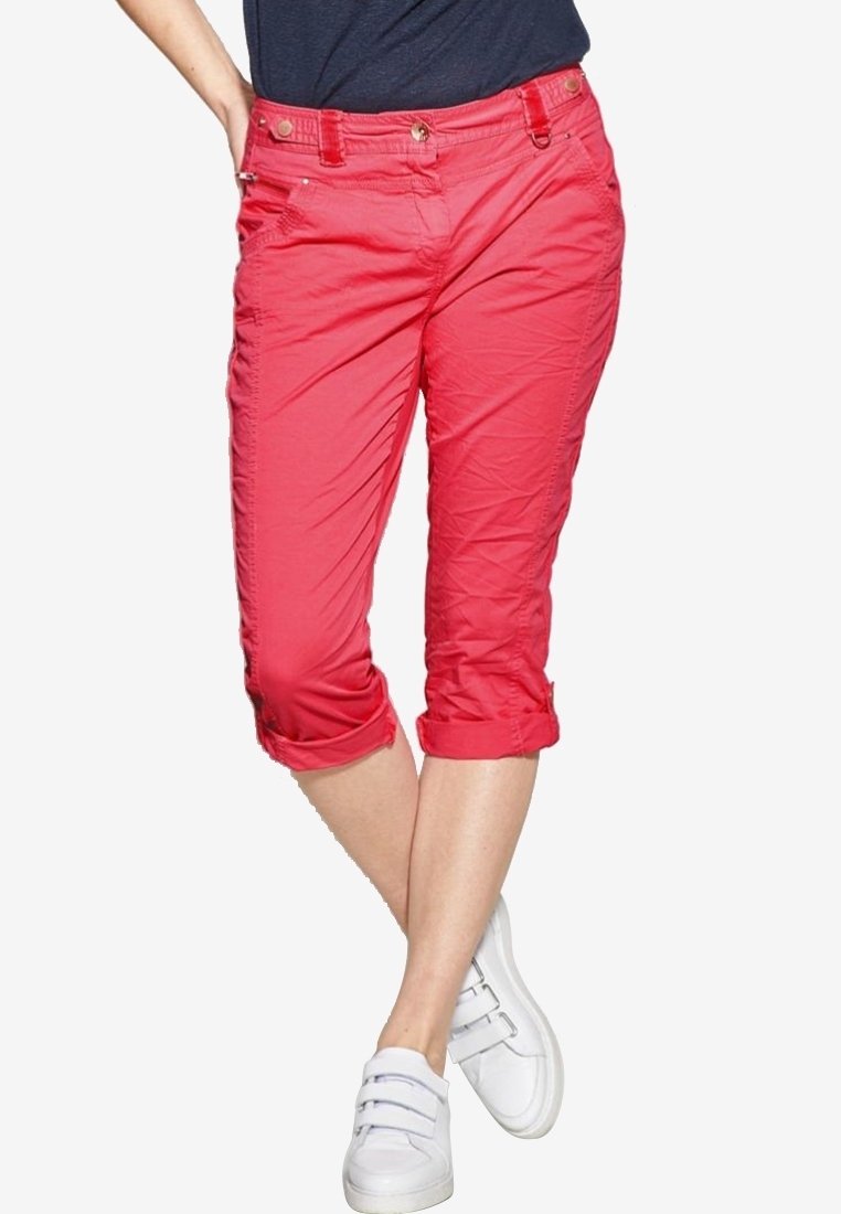 Pink cropped pants with rolled cuffs, featuring front pockets and a smooth texture. Worn with white sneakers for a casual look.