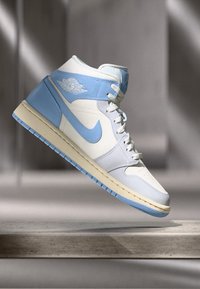 Magas szárú sportcipők, fehér bőr felsőrésszel, világoskék akcentusokkal, texturált középtalppal, kék swoosh-szal és logóval a nyakrészen.