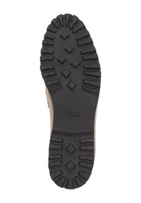 Semelle en caoutchouc noir robuste avec des rainures profondes et des motifs en forme de diamant sur une chaussure beige, vue par le dessous.