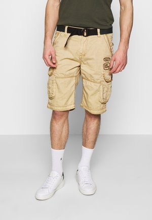 Beige cargoshorts met meerdere zijzakken, versterkte stiksels en een zwarte riem. Gecombineerd met witte sokken en sneakers.