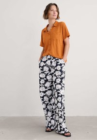 Korte mouwen oranje overhemd met knopen, gecombineerd met losse zwarte en witte bloemenprint broeken; soepel stof, relaxte pasvorm, voorzakken.
