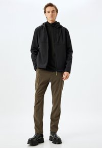 Svart zip-up jacka med två framfickor, parat med mörk olivgröna byxor och svarta klumpiga stövlar. Slät tyg, strukturerad passform.