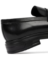 Zapato de cuero negro con un acabado suave, punta redondeada y un ligero tacón; presenta costuras reforzadas y una suela de goma resistente.