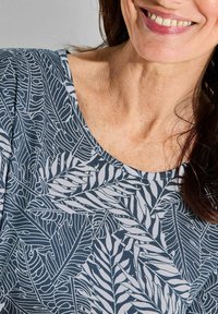 Blauw en witte top met een bladenpatroon. Ronde halslijn. Zachte stof, korte mouwen. Soepele textuur met een ontspannen pasvorm.
