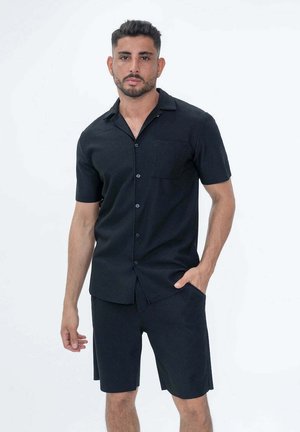 Chemise noire à manches courtes avec un col, fermeture à boutons et poche plaquée ; associée à un short assorti, le tout en tissu texturé.