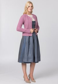Helle rosa gestrickte Strickjacke mit strukturierten Musterdetails, kombiniert mit einem knielangen dunkelblauen Faltenkleid und beigen High Heels.
