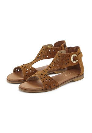 Braune Wildledersandalen mit geometrischen Ausschnitten, offener Zehenpartie, Knöchelriemen und kreisförmigem goldenen Hardware-Akzent, flacher Sohle und brauner Innensohle.