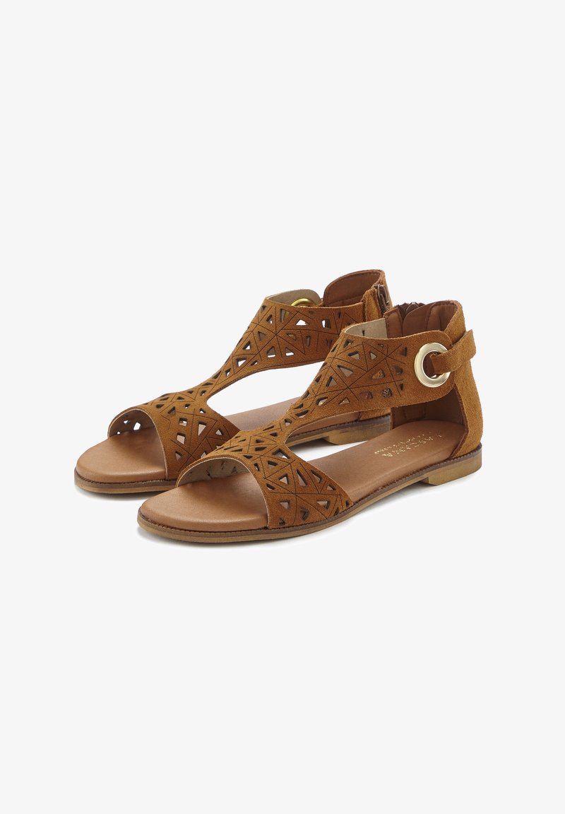 Braune Wildledersandalen mit geometrischen Ausschnitten, offener Zehenpartie, Knöchelriemen und kreisförmigem goldenen Hardware-Akzent, flacher Sohle und brauner Innensohle.