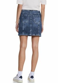 Jeanskjol med mörk tvätt, figursydd form och två bakfickor. Den har midjeyttermid och rå kantdetalj, kombinerad med vita sneakers.