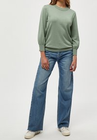 Maglione verde chiaro a maglia con scollatura rotonda e maniche a sbuffo, abbinato a jeans blu a vita alta e gamba larga e sneaker bianche.