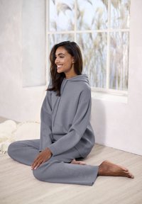 Pilkas džemperis su derančiomis sportinėmis kelnėmis, pagamintas iš minkštos medžiagos. Yra kengūrų kišenė, banguoti rankogaliai ir subtilus ženklinimas ant kelnių.