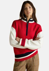 Rot-weißer Strickpullover mit hohem Kragen, ausgestattet mit einem Reißverschluss und marineblauen Streifenakzenten an den Ärmeln und dem Saum. Strukturiertes Gewebe.