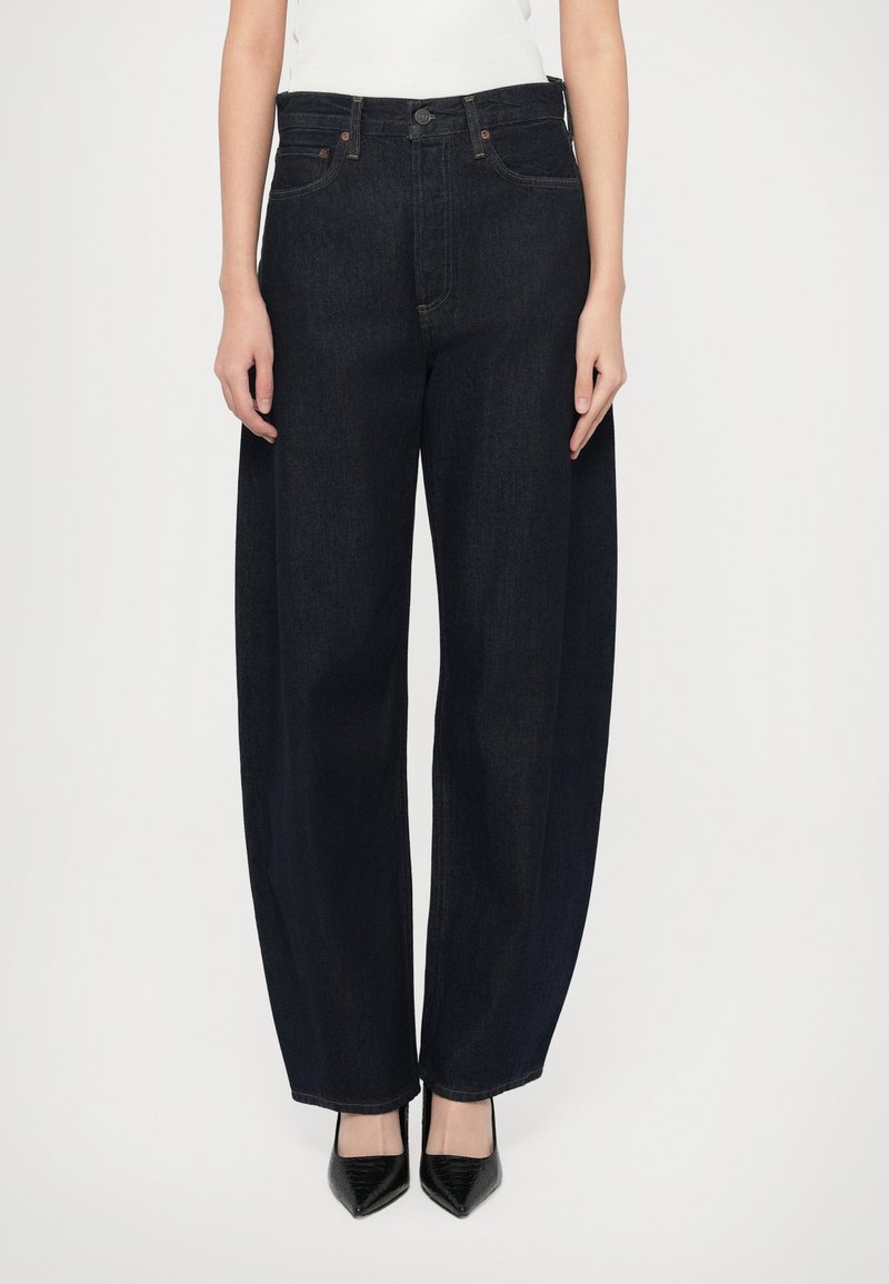 Klasické džíny z tmavého denimu širokého strihu s vysokým pásom, vybavené prednými vreckami, zapínaním na gombík a čistým prešitím. Kombinované s čiernymi špicatými opätkami.