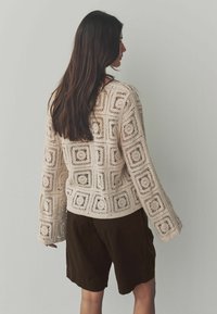 Stickad tröja med rutmönster i beige, med långa ärmar och rund hals, i kombination med mörkbruna shorts.