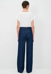 Top bianco a maniche corte abbinato a pantaloni in denim blu scuro a vita alta e gamba larga, caratterizzati da una texture liscia e dettagli di cucitura sottili.