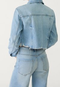 Kort denimjacka i ljusblått med fransad nederkant, har en klassisk krage, långa ärmar och detaljer i ryggen. Matcher med högmidjade jeans.