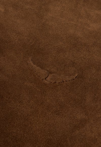 Superfície de camurça castanha com textura suave, apresentando um desenho subtil de asas em relevo. Sem detalhes adicionais ou ferragens visíveis.