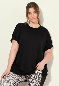 T-shirt nero a maniche corte con risvolti, abbinato a leggings leopardati chiari con accenti viola e un design aderente.