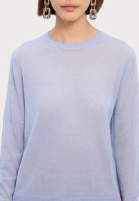 Un pull bleu clair en tissu doux, présentant un col rond et des manches longues avec des détails côtelés à l'ourlet.