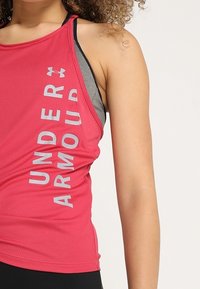 Pinkes Sport-Top mit "UNDER ARMOUR" in grauer Schrift an der Seite, mit schwarzer Mesh-Unterlage für Textur und Atmungsaktivität.