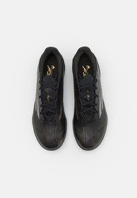 Zapatillas deportivas negras con un upper texturizado, que presentan un diseño elegante, acentos dorados en contraste y cordones negros. Punta redondeada y perfil bajo.
