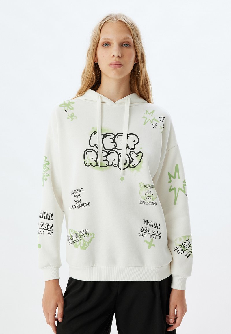 Hvid hoodie med grønne og sorte grafiske prints, der inkluderer tekst og tegneserie detaljer. Den har lange ærmer, en frontlomme og en snorehætte.