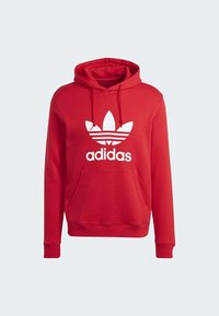 Červená mikina Adidas s kapucí, bílým logem trefoil a přední kapsou klokankou, s táhlem na kapuci a žebrovanými manžetami.