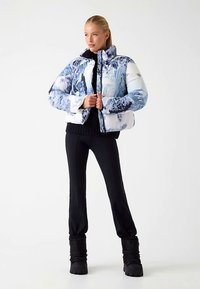 Gewatteerd jack met een blauw-wit abstract patroon, voorzien van een hoge kraag, ritssluiting en een losse pasvorm. Draagt over een zwarte top en broek.