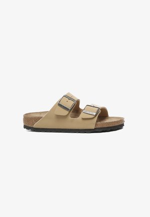 Sandalia deslizante beige con dos hebillas ajustables, plantilla de corcho y suela de goma negra texturizada. Diseño minimalista con punta abierta.