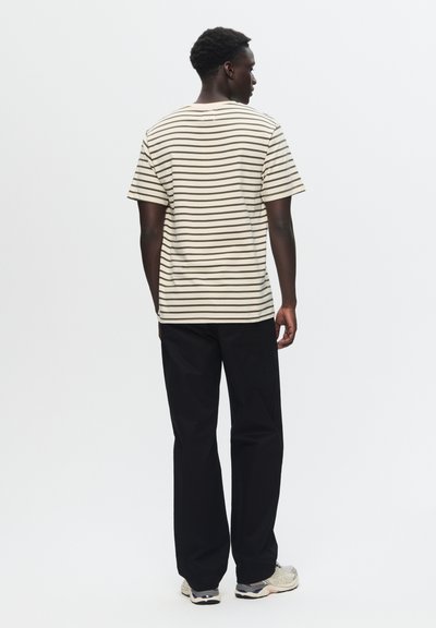 Striped short-sleeve t-shirt in beige and brown, paired with loose black pants. The design features a relaxed fit and soft texture.