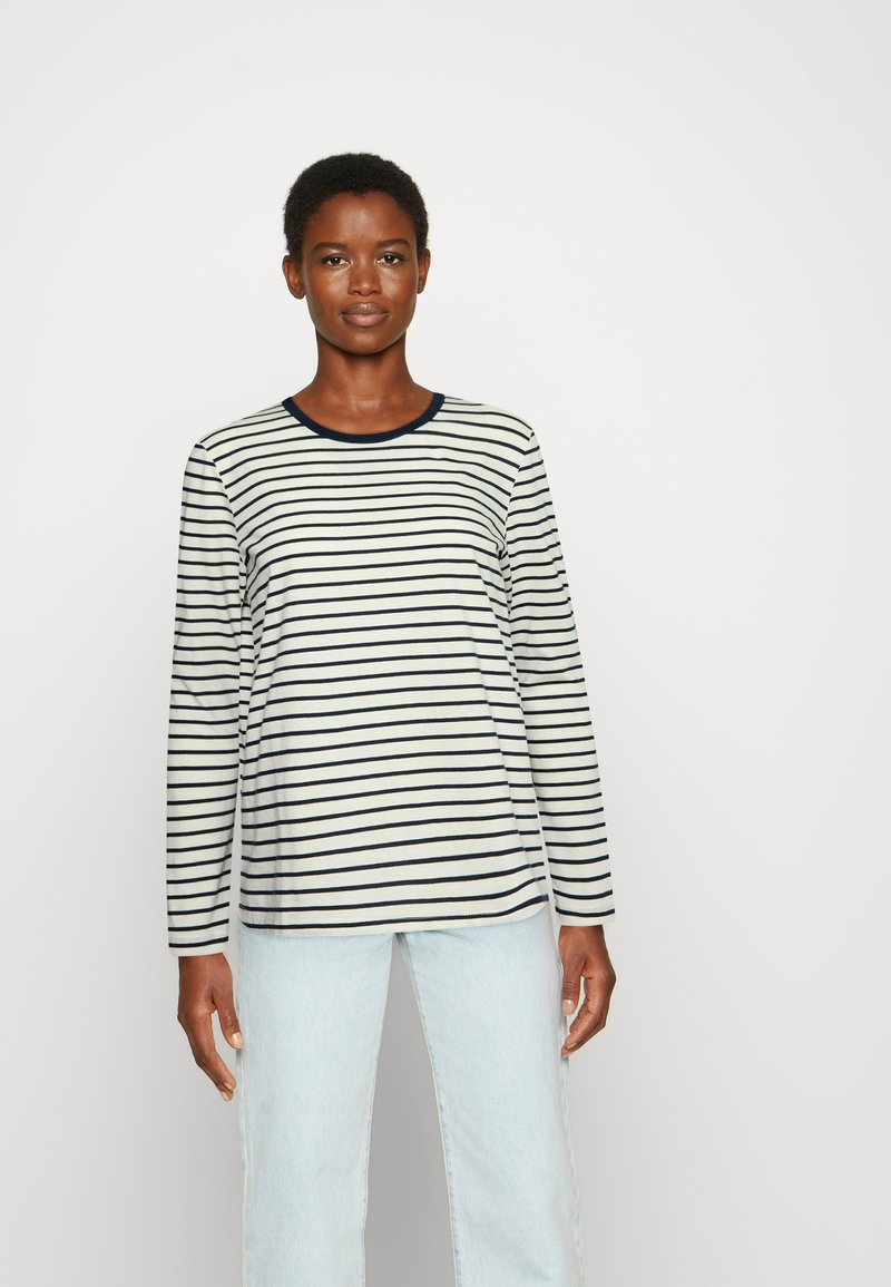 Camisa de manga longa riscada em creme e azul-marinho, com decote arredondado e corte relaxado, combinada com jeans de lavagem clara.