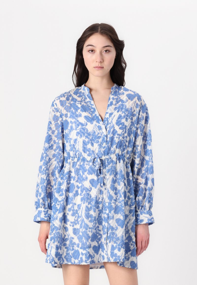 Rochie cu model albastru și alb, cu guler, mâneci lungi și un cordon elastic la talie. Fabricată dintr-un material ușor, cu un finisaj texturat.
