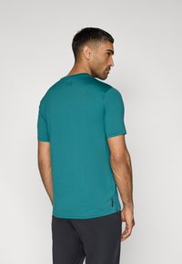 Τιρκουάζ αθλητική κοντομάνικη μπλούζα με στρογγυλή λαιμόκοψη και επίπεδες ραφές, με λογότυπο στο πίσω μέρος και διακριτική υφή.