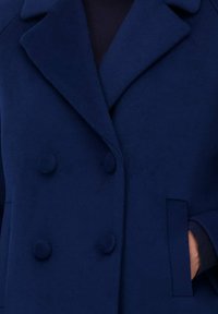 Marineblauwe wollen jas met dubbele knopen, grote revers en gestructureerde stof. Bevat zijzakken en ribgebreide manchetten.