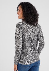 Chemise à manches longues en imprimé léopard beige et noir, dotée d'une coupe décontractée et de détails de boutons au dos, associée à un jean en denim bleu.