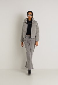 Grå pufferjakke med cropped design, parret med grå brede bukser og sort top. Modellen bærer sølvsolbriller og sorte stiletter.