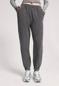 Szare dresy wykonane z miękkiego materiału, z elastycznym pasem, bocznymi kieszeniami i zwężanymi mankietami. W połączeniu z srebrnymi butami sportowymi.