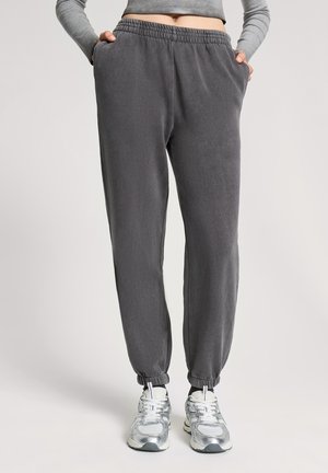 Pantaloni jogger grigi realizzati in tessuto morbido, con vita elastica, tasche laterali e polsini a forma affusolata. Abbinati a scarpe sportive argentate.