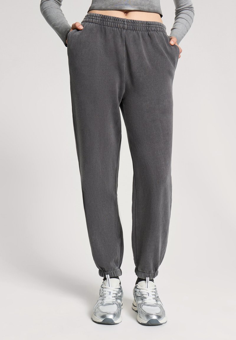 Szare dresy wykonane z miękkiego materiału, z elastycznym pasem, bocznymi kieszeniami i zwężanymi mankietami. W połączeniu z srebrnymi butami sportowymi.